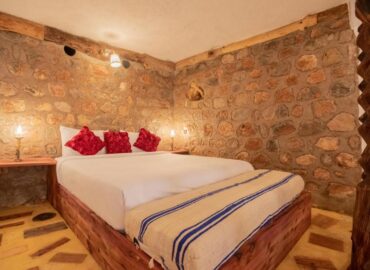 Family Suite bedroom with stone walls, wooden bed frame and red decorative pillows at Dar l'Eau Vive guest house