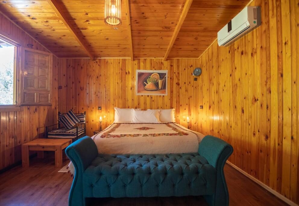 Bungalow Double bedroom with wood-paneled walls and teal tufted bench at Dar l'Eau Vive guest house